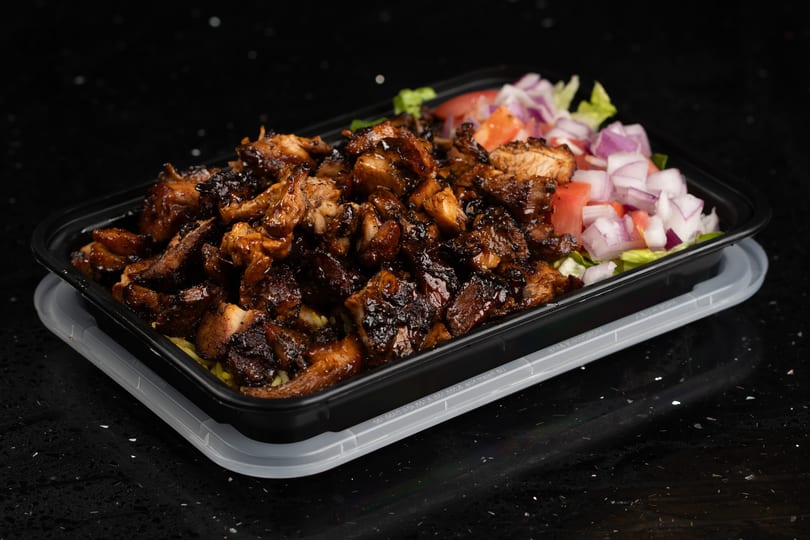 A black takeout container filled with dark glazed chicken, rice, and a side salad.