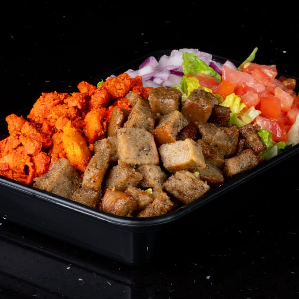 Takeout container with red chicken, brown meat, red onions, lettuce, and diced tomatoes on a black surface.