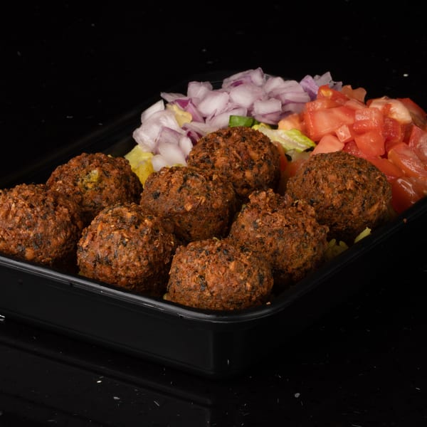 A black tray filled with falafel, diced tomatoes, and red onions on a dark surface.